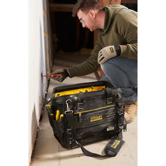 Photo du sac à outils STANLEY FMST17627-1 avec accents jaunes, rempli d’outils à main, posé sur un sol de chantier.