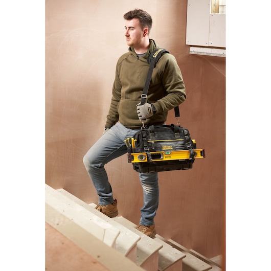 Sac à outils STANLEY FMST17627-1 avec sangle et outils attachés, porté par une personne sur des escaliers.