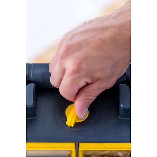 STANLEY FMST81077-1 boîte à outils en gros plan, main tournant le loquet jaune sur le couvercle noir.