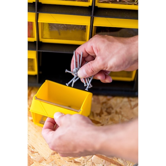 Photo du bac de rangement jaune STANLEY FMST81077-1 en utilisation, contenant des clous, main déposant les clous dedans.