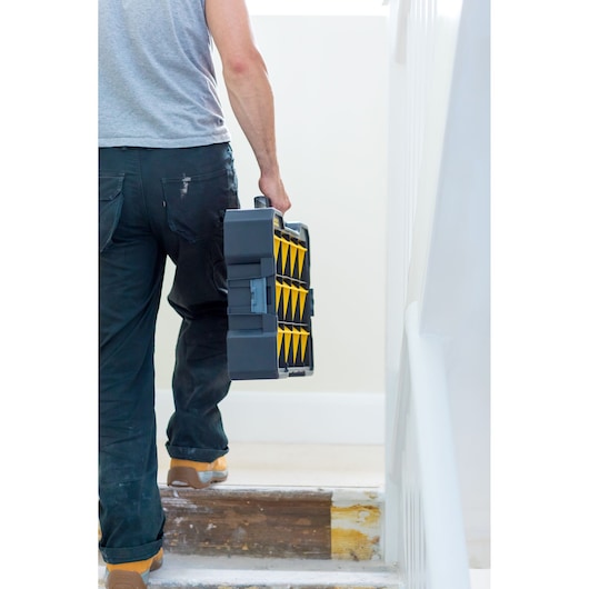 Photo d'une personne transportant un organiseur d’outils STANLEY FMST81077-1 avec des compartiments jaunes dans un escalier.