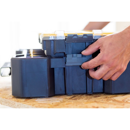 Boîte organisatrice STANLEY FMST81077-1 avec couvercle jaune, vue latérale, main ouvrant le loquet.