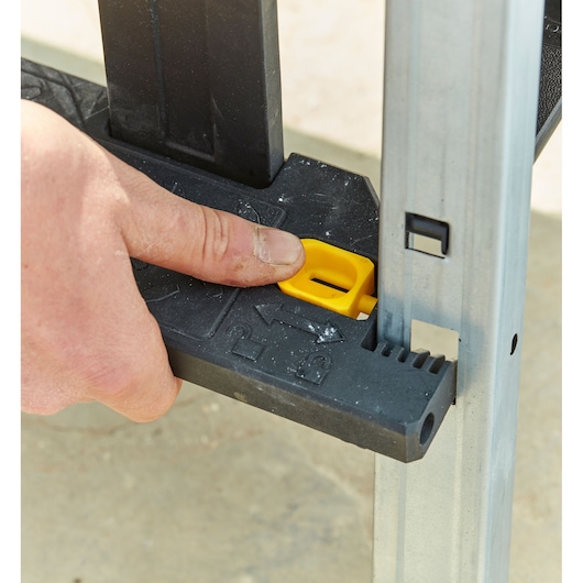 STANLEY FMST81083-1 werkbank close-up, hand drukt gele vergrendelknop op zwarte steun in.