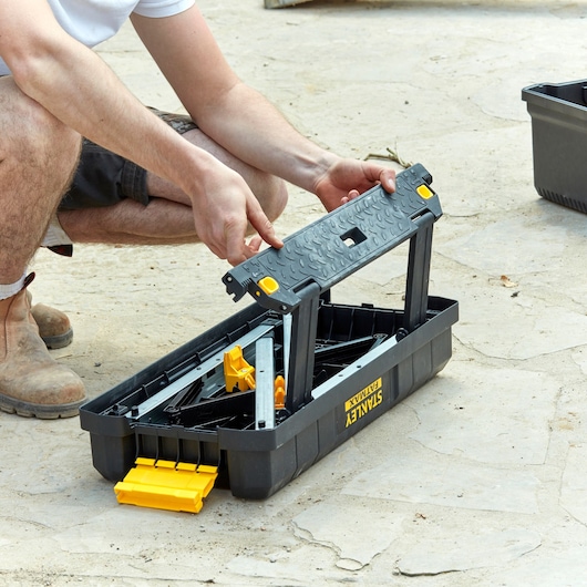 STANLEY FMST81083-1 zwart-gele opvouwbare gereedschapskoffer met handvat, deels geopend buitenshuis getoond.