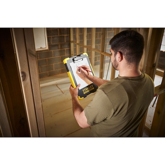Photo du clipboard STANLEY FMST82721-1 tenu sur chantier, avec design jaune et noir robuste.
