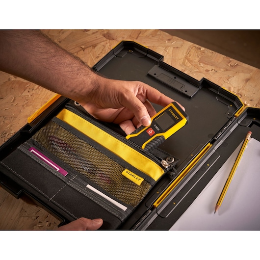 Photo de la mallette à outils STANLEY FMST82721-1 avec organiseur jaune et noir, main tenant un outil de mesure numérique.