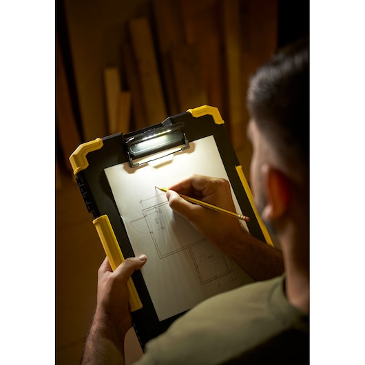 STANLEY FMST82721-1 planchette à pince avec lampe LED, vue de dessus en utilisation, crayon en main et plans dessinés.