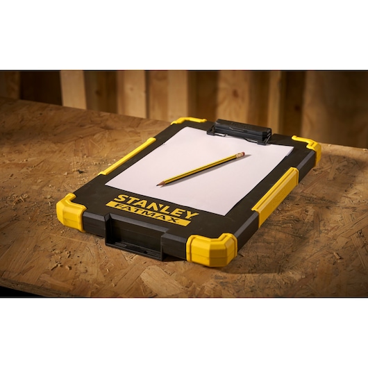 STANLEY FMST82721-1 clipboard avec coins jaunes, crayon et papier, vue en angle sur table en bois.