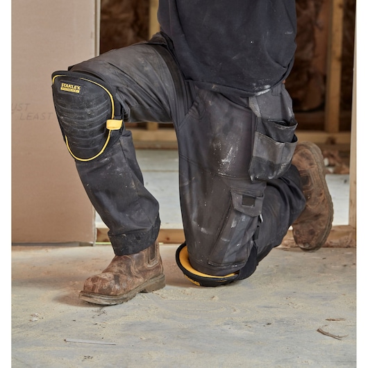 STANLEY FMST82959-1 zwart-gele kniebeschermer gedragen door iemand die knielt op een bouwplaats.