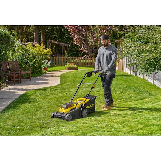 Photo de la tondeuse à gazon STANLEY SCMWP3701M2 utilisée sur une pelouse verte, dans un jardin extérieur.