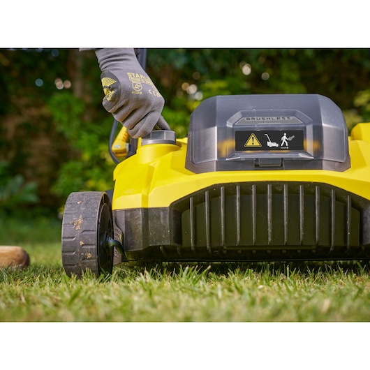 Stanley SCOEP3801N grasmaaier vooraanzicht met gehandschoende hand die hoogte aanpast in tuin.