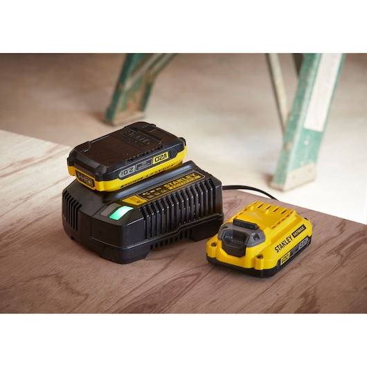 Foto van STANLEY SFMCB12D2 acculader en accupack in geel en zwart op een houten oppervlak.