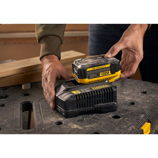 Foto van STANLEY SFMCB14M1 18V lithium-ion accu die op lader wordt geplaatst, op een werkbank.