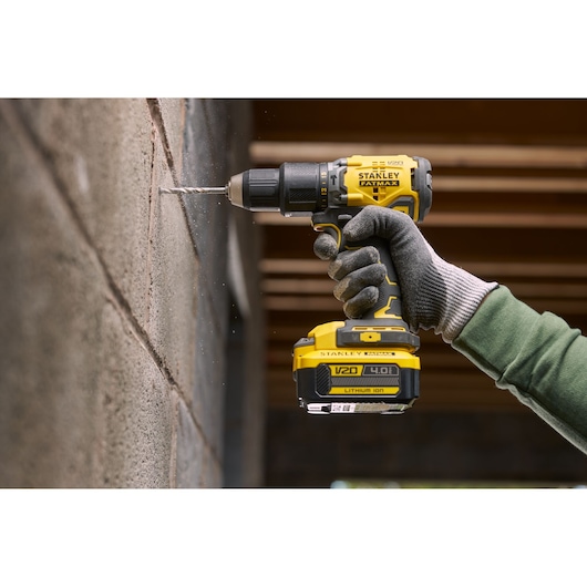 STANLEY SFMCB14M1 snoerloze boormachine in gebruik, boort in betonnen muur, close-up van gereedschap en gehandschoende hand.