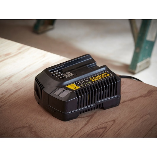 Foto van STANLEY SFMCB14 zwarte acculader op houten oppervlak, met FATMAX-label, in werkplaats.