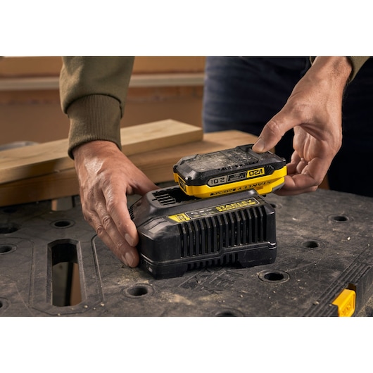 STANLEY SFMCB202 accu wordt op zwarte oplader geplaatst, close-up met werkbank op de achtergrond.