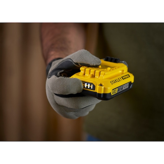 Foto van een gehandschoende hand met een STANLEY V20 2.0Ah accu, SKU SFMCB202, gereedschapaccessoire.