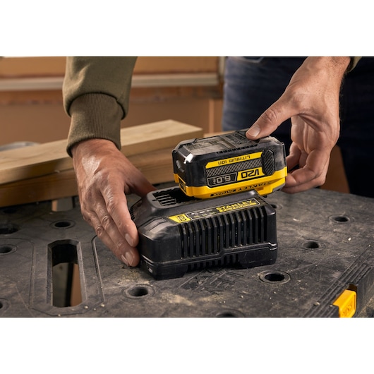 STANLEY SFMCB206 batterij wordt op oplader geplaatst, close-up op zwart werkoppervlak.