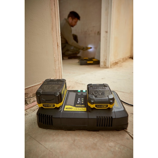 STANLEY SFMCB24 duale lader met twee V20 accu's op de vloer in een bouwomgeving.