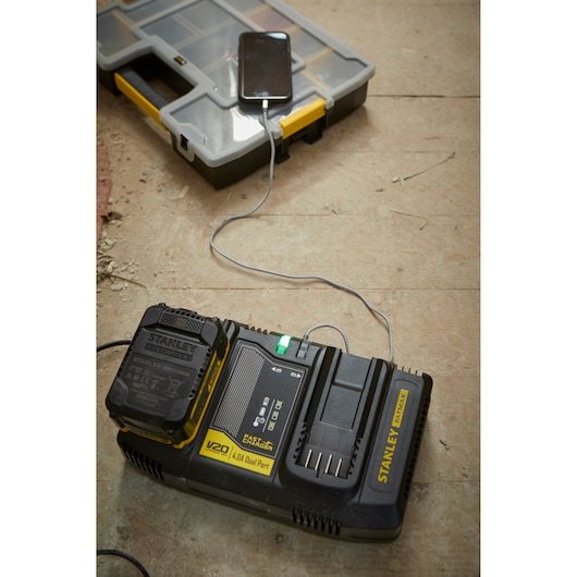 STANLEY SFMCB24 dubbele batterijoplader laadt een apparaat op, op werkplaatsvloer, hoekaanzicht.