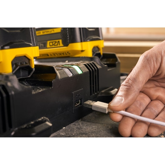 STANLEY SFMCB24 acculader close-up met USB-poort, hand steekt USB-kabel in, deels batterij zichtbaar.