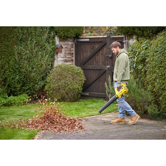 Foto van persoon die STANLEY SFMCBL714M1 draadloze bladblazer gebruikt om bladeren van het tuinpad te blazen.