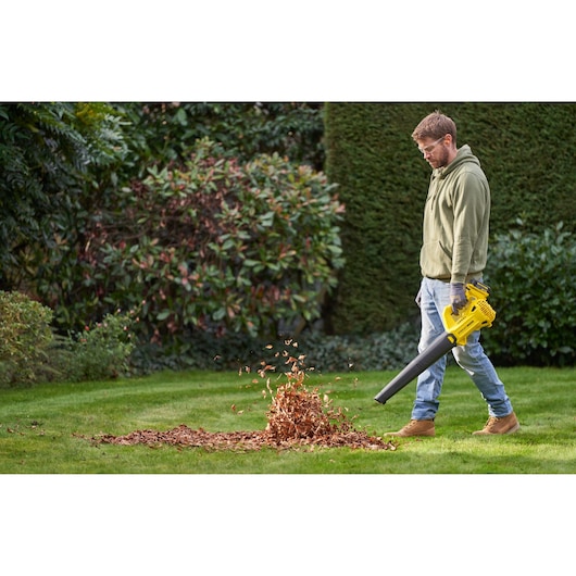 STANLEY SFMCBL714M1 bladblazer in gebruik buiten, blaast bladeren op een groen gazon.