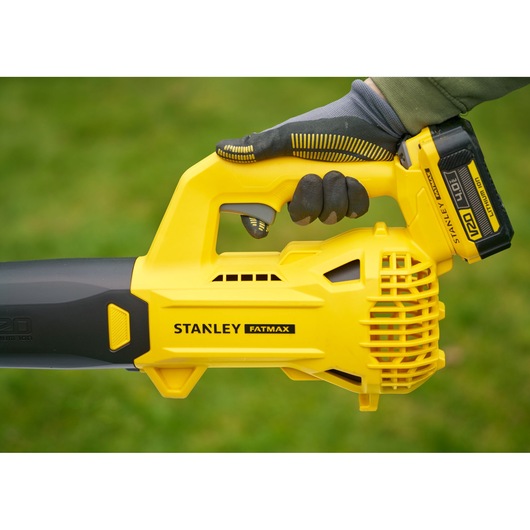 STANLEY SFMCBL714M1 gele draadloze bladblazer in hand, zijaanzicht, gras op de achtergrond.