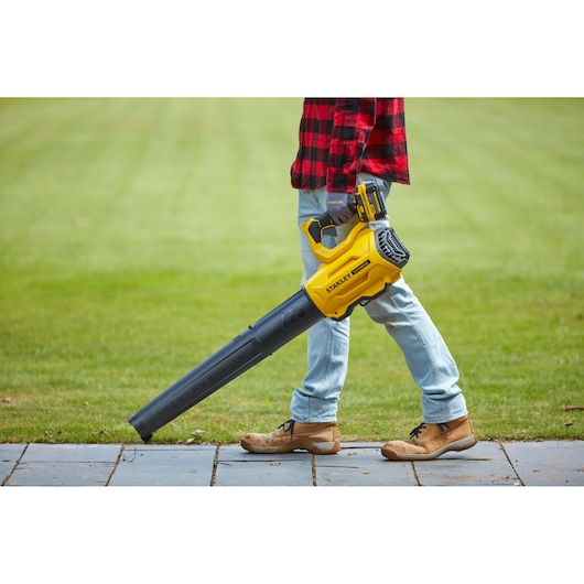 Stanley SFMCBL7B bladblazer, vastgehouden door persoon buiten op gras, met jeans en boots.