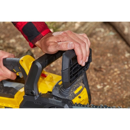 STANLEY SFMCCS630B tronçonneuse gros plan, mains tenant la poignée noire, corps jaune visible.
