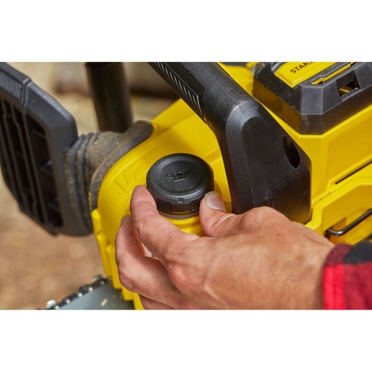 STANLEY SFMCCS630M1 tronçonneuse gros plan, main réglant le bouchon d'huile, design jaune et noir, extérieur.
