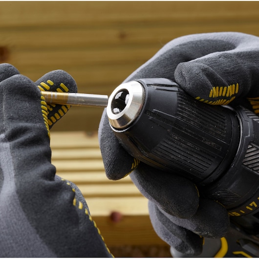 STANLEY SFMCD700C2K perceuse en gros plan avec des mains gantées insérant un foret métallique, extérieur.