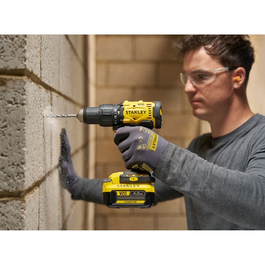Persoon boort met STANLEY V20 accuboor in een muur op een bouwlocatie.