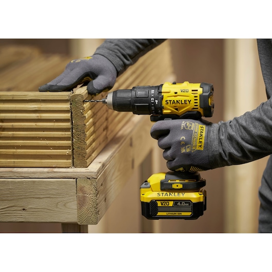 Persoon gebruikt een Stanley V20 accuboor om houten planken te boren, met handschoenen aan.