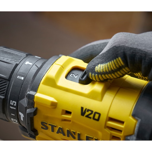 Close-up van een hand met handschoen die de snelheid van een gele STANLEY V20 boormachine aanpast.