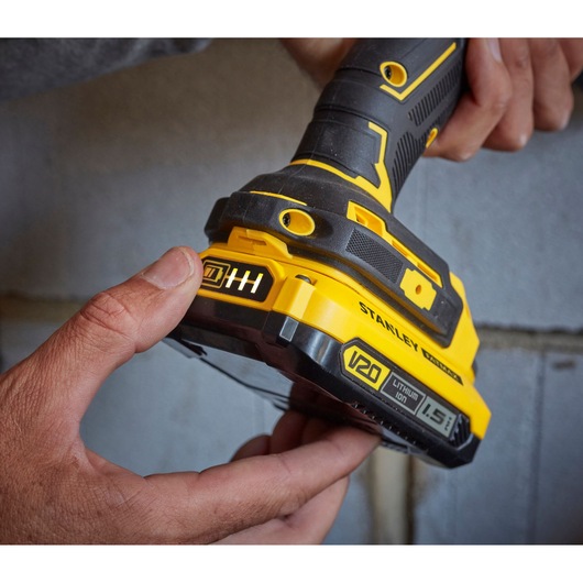 Stanley SFMCD715C2K V20 draadloze boormachine close-up met hand, gele en zwarte grip en batterij.