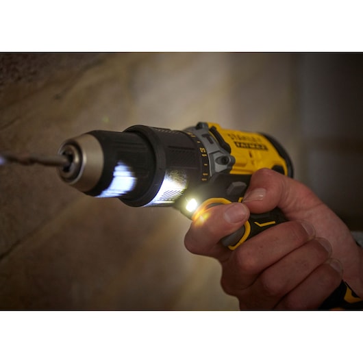 STANLEY SFMCD715C2K draadloze boormachine met LED-licht, close-up boren in muur, geel en zwart ontwerp.