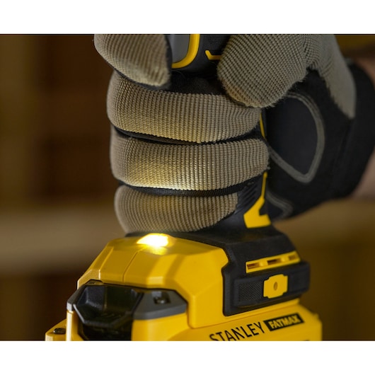 Photo d'une main gantée tenant une perceuse sans fil STANLEY SFMCD720D2K avec lumière LED allumée, vue rapprochée.