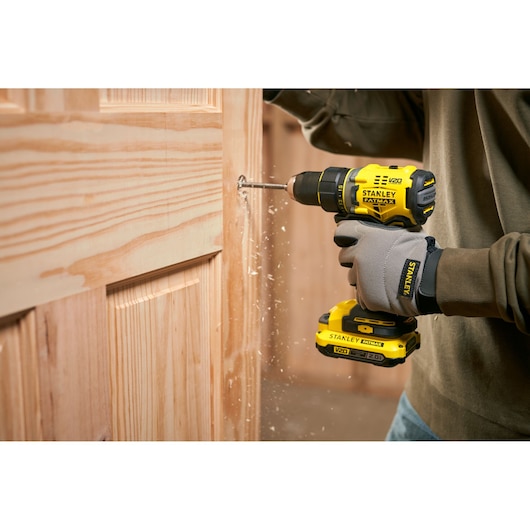 Photo de la perceuse sans fil STANLEY SFMCD720D2K utilisée pour percer une porte en bois, vue rapprochée.