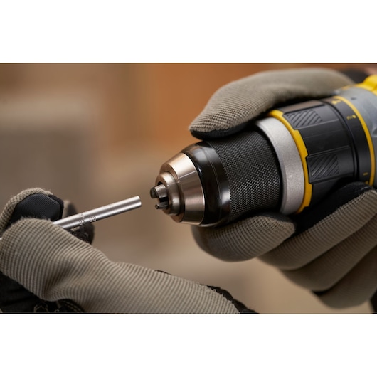 Foto van STANLEY SFMCD721B draadloze boormachine met metalen bit, close-up, handschoenen zichtbaar.