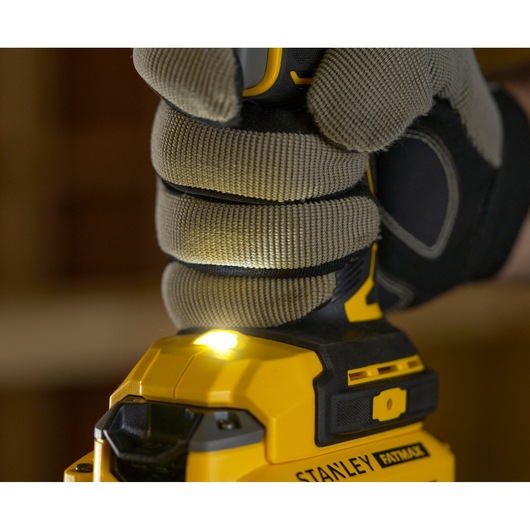 Foto van STANLEY SFMCD721B boormachine, vastgehouden door een gehandschoende hand, LED-werklicht aan, close-up.