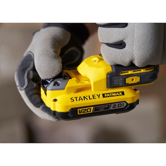 Close-up foto van STANLEY SFMCD721B gereedschap met gele FATMAX V20 2.0Ah lithium-ion accu vastgehouden door gehandschoende handen.