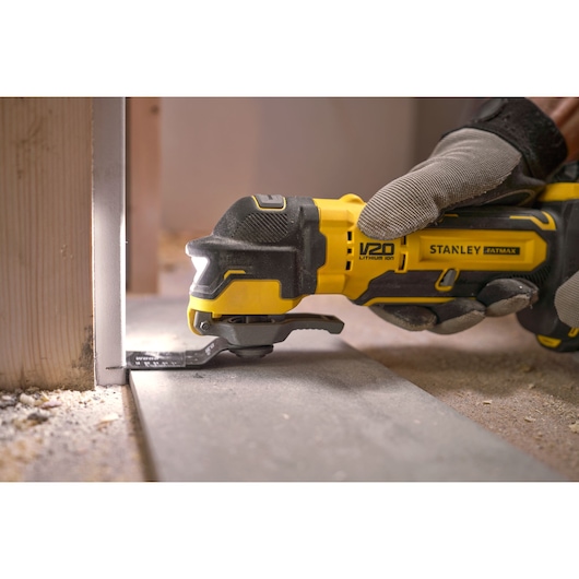 STANLEY SFMCE510B multitool snijdt dicht bij de muur, geel-zwart, zijaanzicht, bouwomgeving.