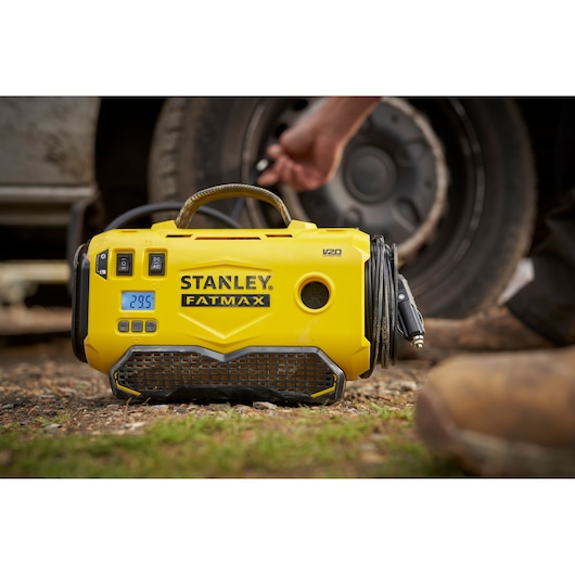 STANLEY SFMCE520B gele draagbare bandenpomp met digitaal scherm, getoond naast een autoband buiten.