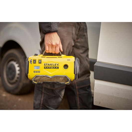 Stanley SFMCE520B draagbare gele compressor aan handvat, buiten bij een voertuig.