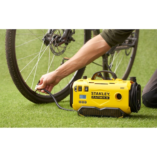 STANLEY SFMCE520B draagbare inflator in gebruik, een fietsband oppompend op groen gras, vooraanzicht.