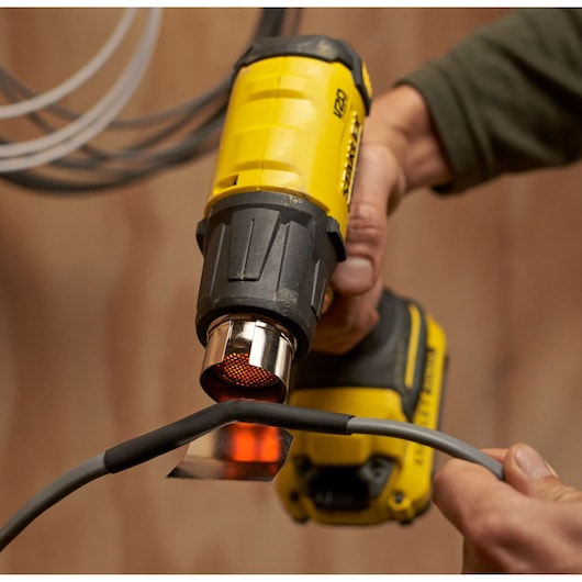 Photographie du pistolet à air chaud sans fil STANLEY SFMCE530B utilisé pour chauffer un câble.