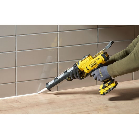 STANLEY SFMCE600B pistolet à calfeutrer sans fil utilisé pour sceller un joint entre un plan de travail en bois et un mur carrelé.