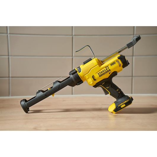 Stanley SFMCE600B pistolet à mastic sans fil, vue latérale, jaune et noir, posé sur surface en bois.