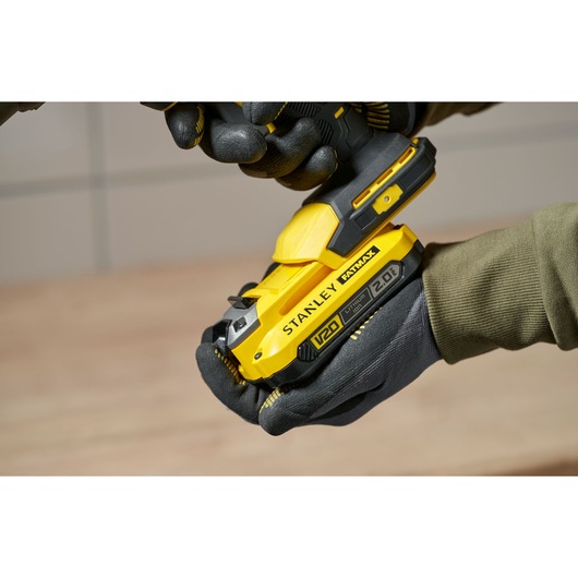 Photo de l'outil sans fil jaune STANLEY SFMCE600B tenu par des mains gantées, vue latérale rapprochée.